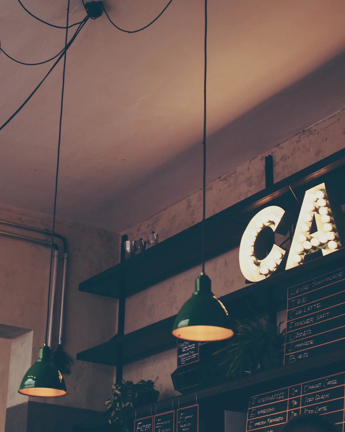 Akşam ışıkları yanan bir kafenin tezgâhı ve duvardaki CAFE tabelası